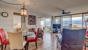 A spacious living area with a dining table, chairs, a television, and a view of the ocean. - Wake, Sip and Savor the Views in Your 2BR Escape (Wailuku)