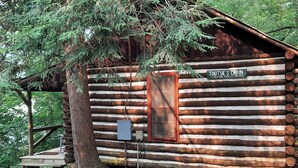 A log cabin named "Tootsie's Cabin" with a wooden exterior, a window, and a small porch area. - Historic one bedroom log cabin (Lake Lure)