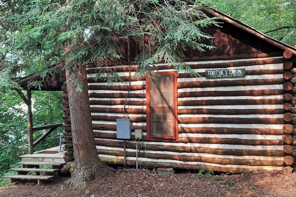 A log cabin named "Tootsie's Cabin" with a wooden exterior, a window, and a small porch area.