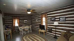 A log cabin interior with a dining table, chairs, a television, a lamp, and a sofa. - Historic one bedroom log cabin (Lake Lure)