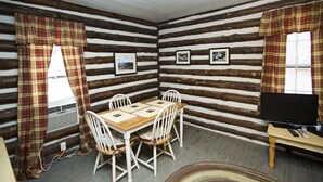 A log cabin room with a wooden table and chairs, a television, and framed pictures on the walls. - Historic one bedroom log cabin (Lake Lure)