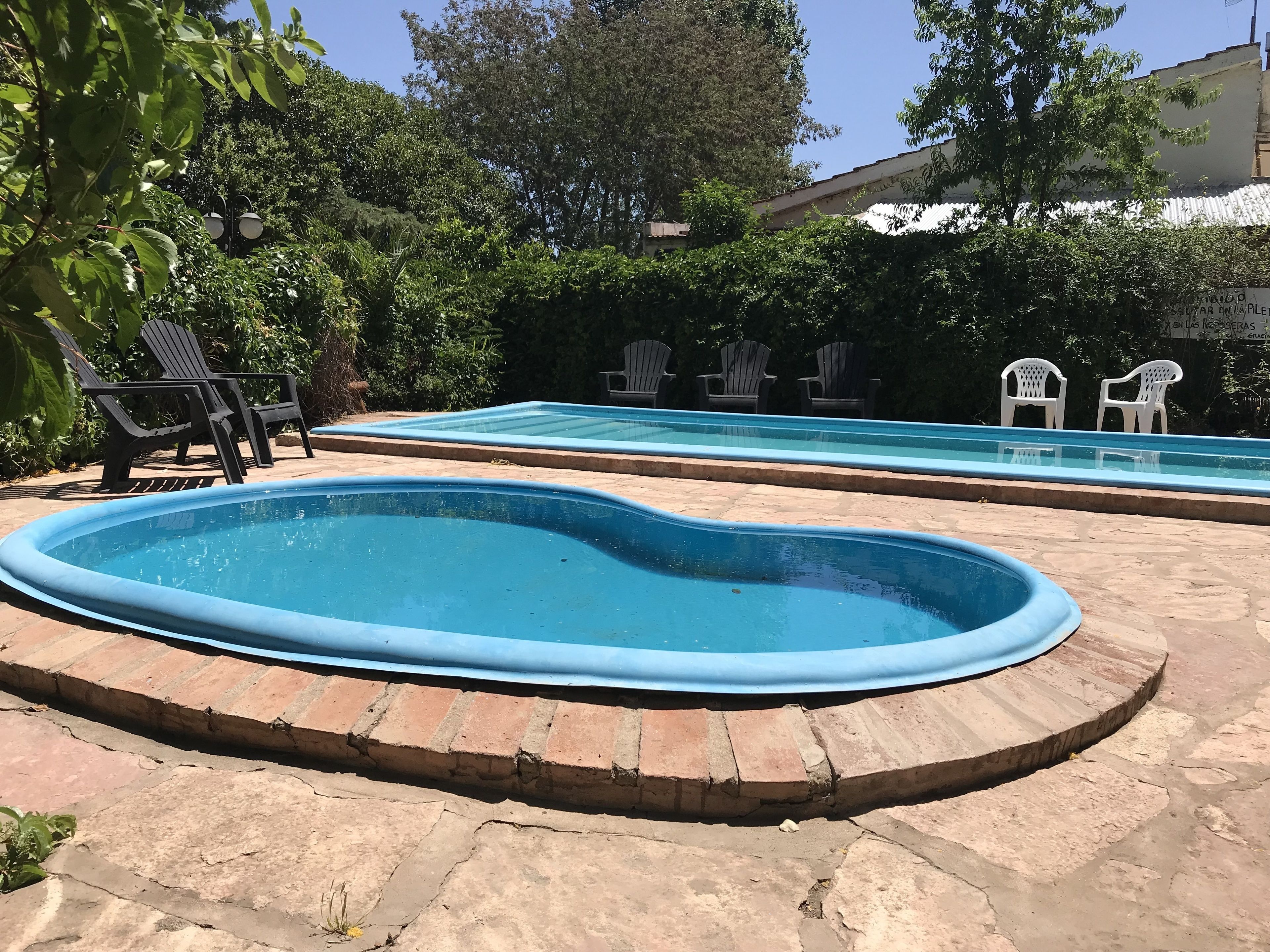 An outdoor swimming pool with a brick border and a smaller inflatable pool in the foreground.