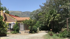 A house with a gravel driveway, a patio with a table and chairs, and a garden with various plants and trees. - Sol y Luna (Los Molles)
