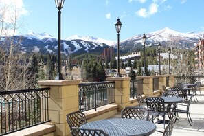 Enjoy mountain views from this outdoor patio with tables and chairs, surrounded by trees and buildings.