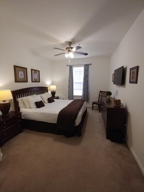 A bedroom with a bed, a ceiling fan, a TV, a dresser, and a window with curtains. - Resort with free waterpark, 1 1/2  miles from Disney! (Kissimmee)