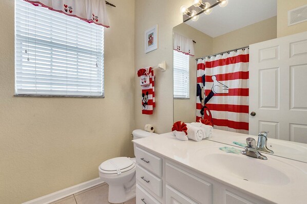A bathroom with a white vanity, a toilet, and a shower curtain with a Mickey Mouse design.