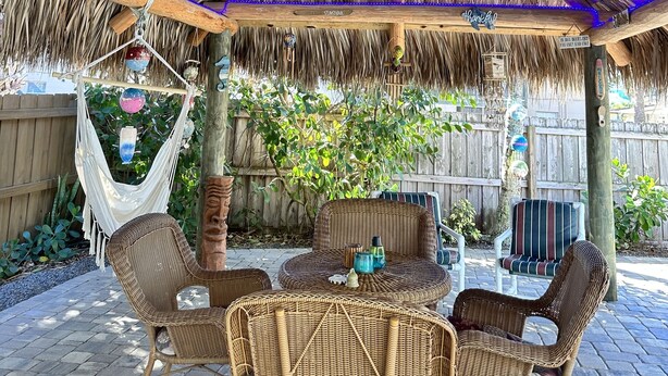 A covered outdoor seating area with wicker furniture, a ceiling fan, and a thatched roof. - Private Beach House Oasis! Heated Pool, Tiki hut, Ocean few houses away (Cape Canaveral)