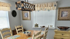 A dining room with a wooden table, white chairs, a chandelier, and a window with blinds. - Private Beach House Oasis! Heated Pool, Tiki hut, Ocean few houses away (Cape Canaveral)