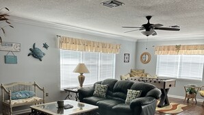A living room with a sofa, coffee table, and ottoman. There is a ceiling fan, a lamp, and a window with blinds. - Private Beach House Oasis! Heated Pool, Tiki hut, Ocean few houses away (Cape Canaveral)