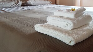 Un lit bien fait, avec du linge de lit blanc, une serviette pliée posée sur le bord et un tableau représentant un arbre accroché au mur.