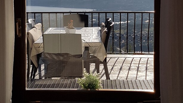 Un balcon avec une table et des chaises, offrant une vue panoramique sur une étendue d’eau et un paysage lointain.