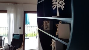 Un salon moderne avec un plafond en bois, une étagère circulaire noire agrémentée d’objets décoratifs, un fauteuil noir et une vue sur l’extérieur.