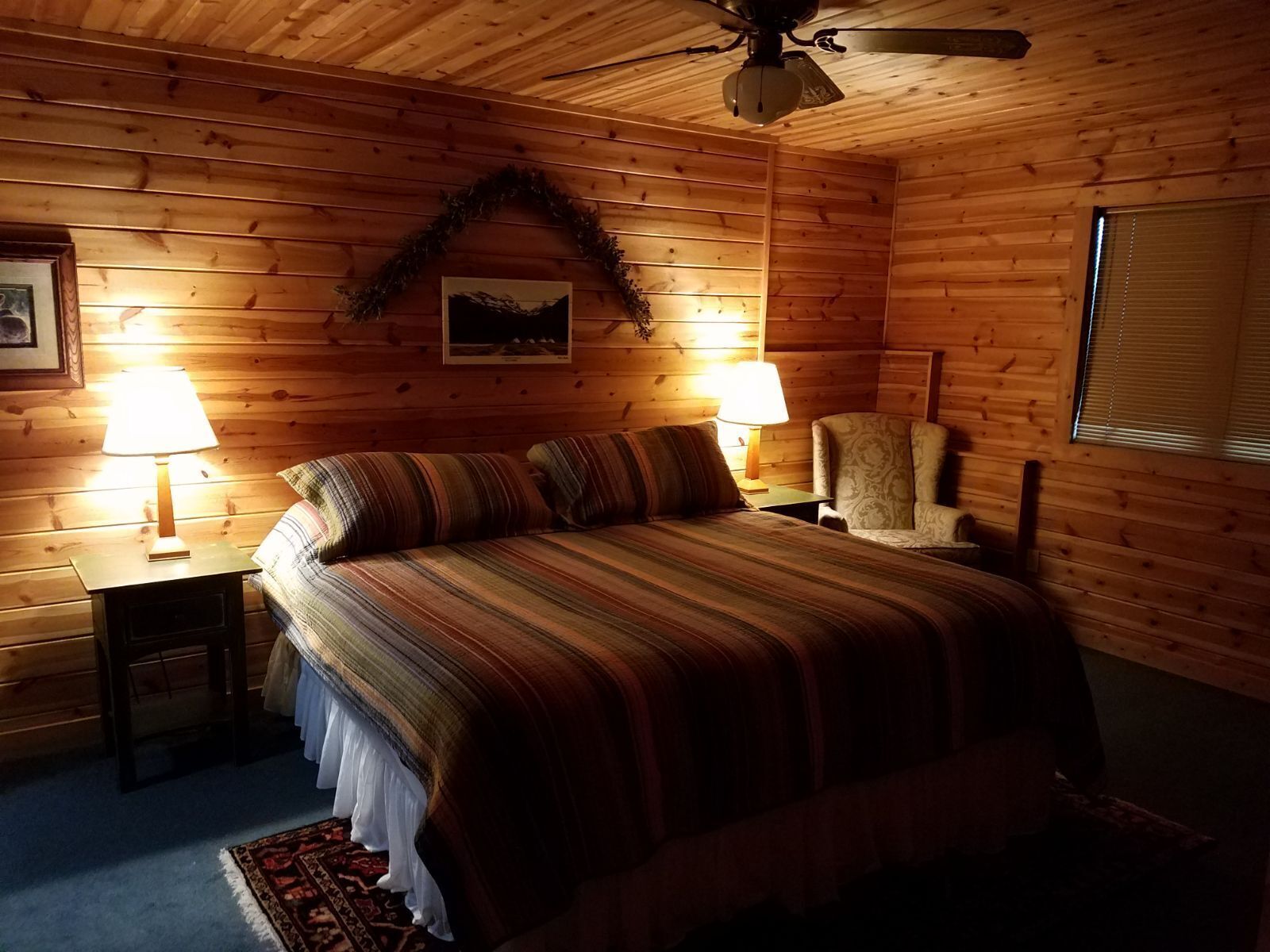 Une chambre confortable, aménagée dans un chalet en bois, avec un lit, deux lampes de chevet, une chaise et un ventilateur de plafond.
