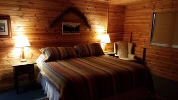 Une chambre confortable, aménagée dans un chalet en bois, avec un lit, deux lampes de chevet, une chaise et un ventilateur de plafond.