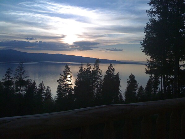 A serene lakeside view with a calm lake, distant mountains, and a forest of tall trees. - Flathead Lake - Bigfork log cabin with stunning views Apartment (Bigfork)