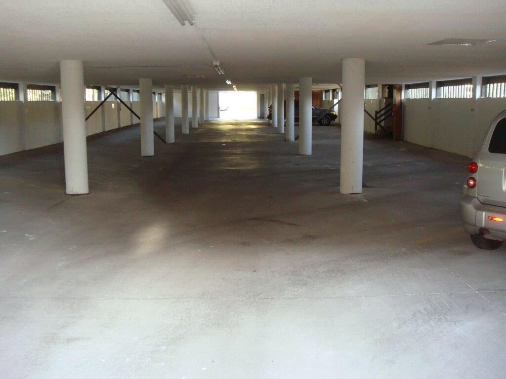 An indoor parking garage with concrete pillars, a car parked on the right, and a staircase leading to an upper level.