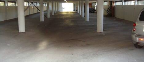 An indoor parking garage with concrete pillars, a car parked on the right, and a staircase leading to an upper level.