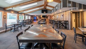 A spacious dining area with high ceilings and exposed beams, featuring multiple tables and chairs.