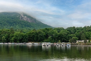 A lake with boats docked, surrounded by dense forest and a mountain in the background.