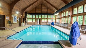 An indoor swimming pool with a wooden ceiling, clear windows, and a lifeguard chair.