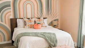 A bedroom with a bed, a bench, a ceiling fan, and a wall with a geometric pattern.