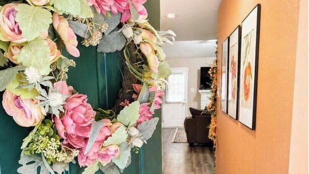 A hallway with a green door adorned with a floral wreath, a patterned rug, and framed pictures on the wall.