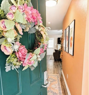 A hallway with a green door adorned with a floral wreath, a patterned rug, and framed pictures on the wall. - The Peach Club - Across from the Augusta National (Augusta)