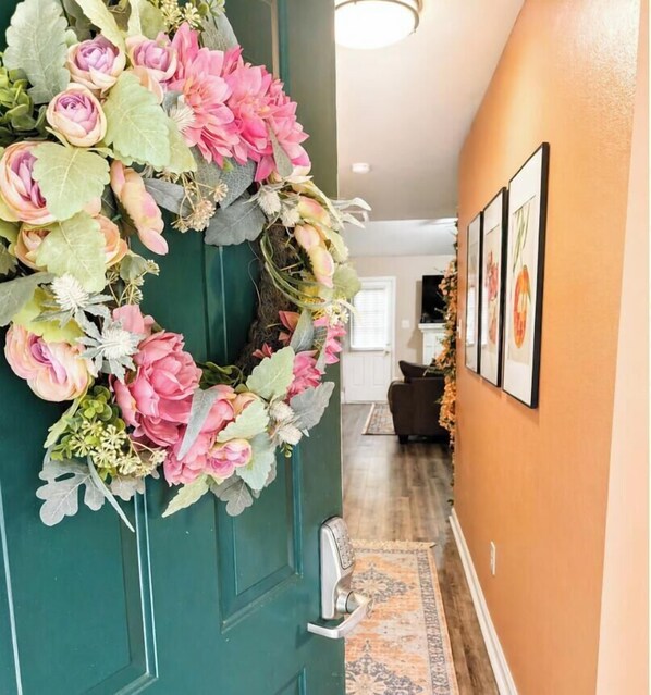 A hallway with a green door, a floral wreath, a patterned rug, and framed pictures on the wall. - The Peach Club - Across from the Augusta National (Augusta)