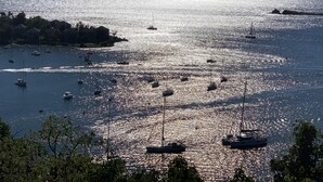 Un puerto deportivo con varias embarcaciones ancladas en aguas tranquilas, rodeado de colinas y un cielo despejado.