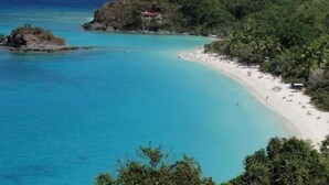Un paisaje costero con playa, aguas azules cristalinas y colinas verdes exuberantes.