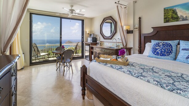 Habitación de hotel con una cama grande, un escritorio con silla, vistas al océano y un balcón.
