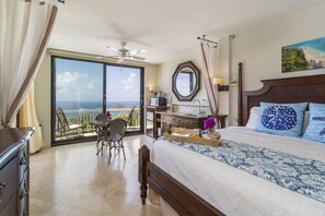 Hotelkamer met een groot bed, een bureau met stoel, uitzicht op de oceaan en een balkon.