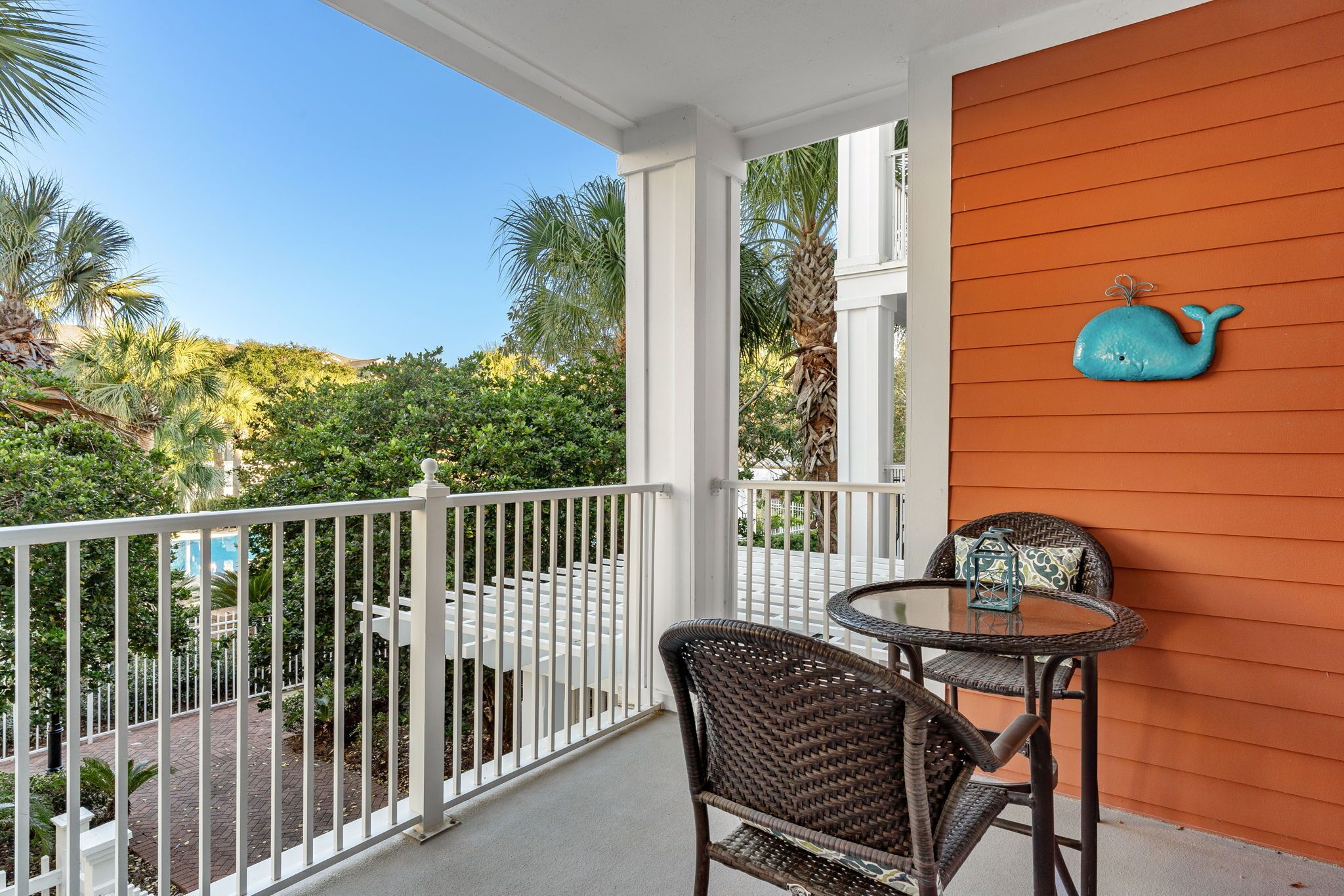 A balcony with a white railing, a wicker chair, a small round table, and a decorative whale wall hanging.