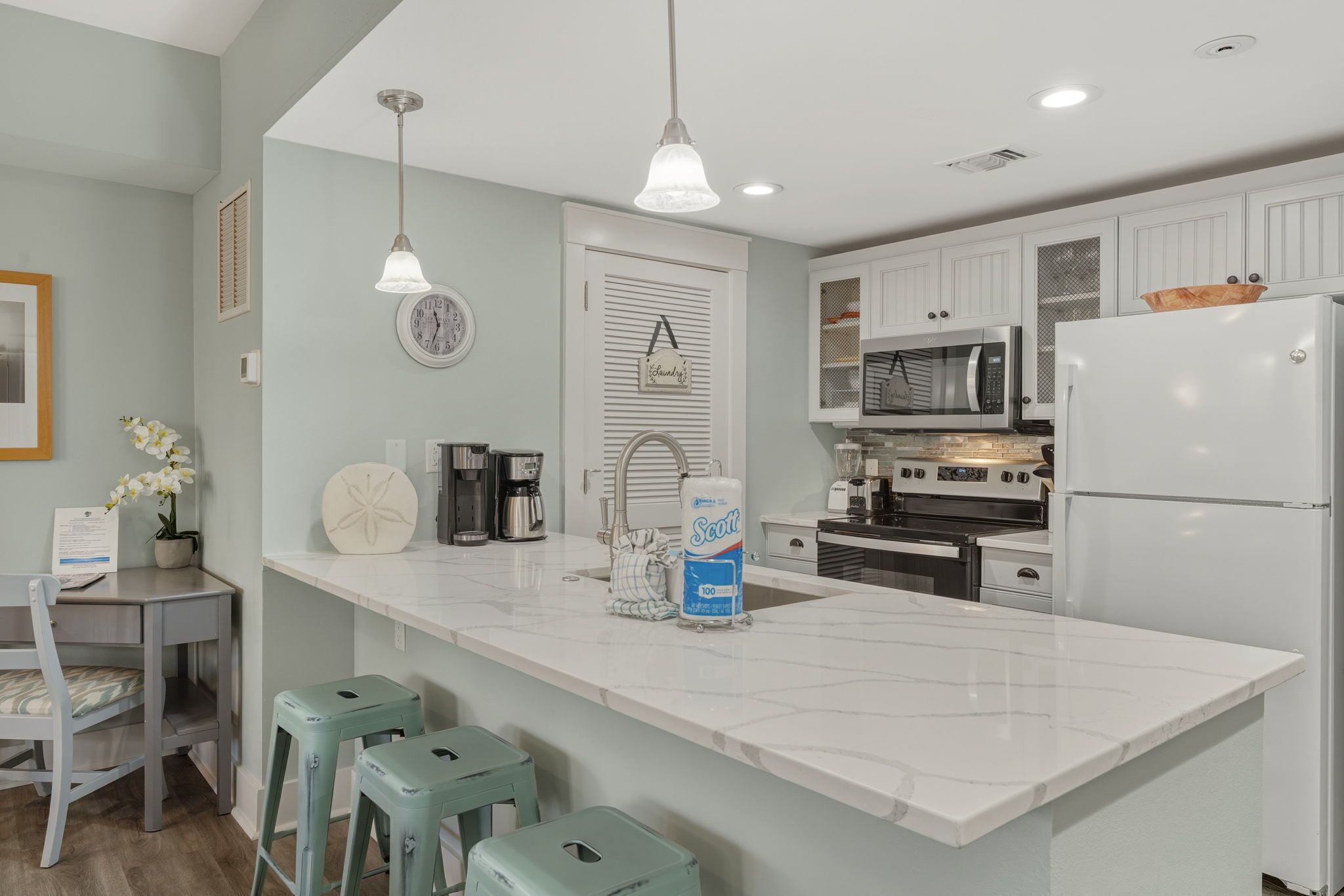 A modern kitchen with white cabinets, a large island, a refrigerator, a microwave, and a sink.