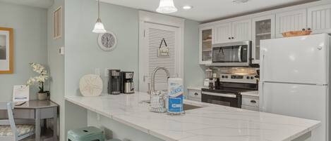 A modern kitchen with white cabinets, a large island, a refrigerator, a microwave, and a sink.