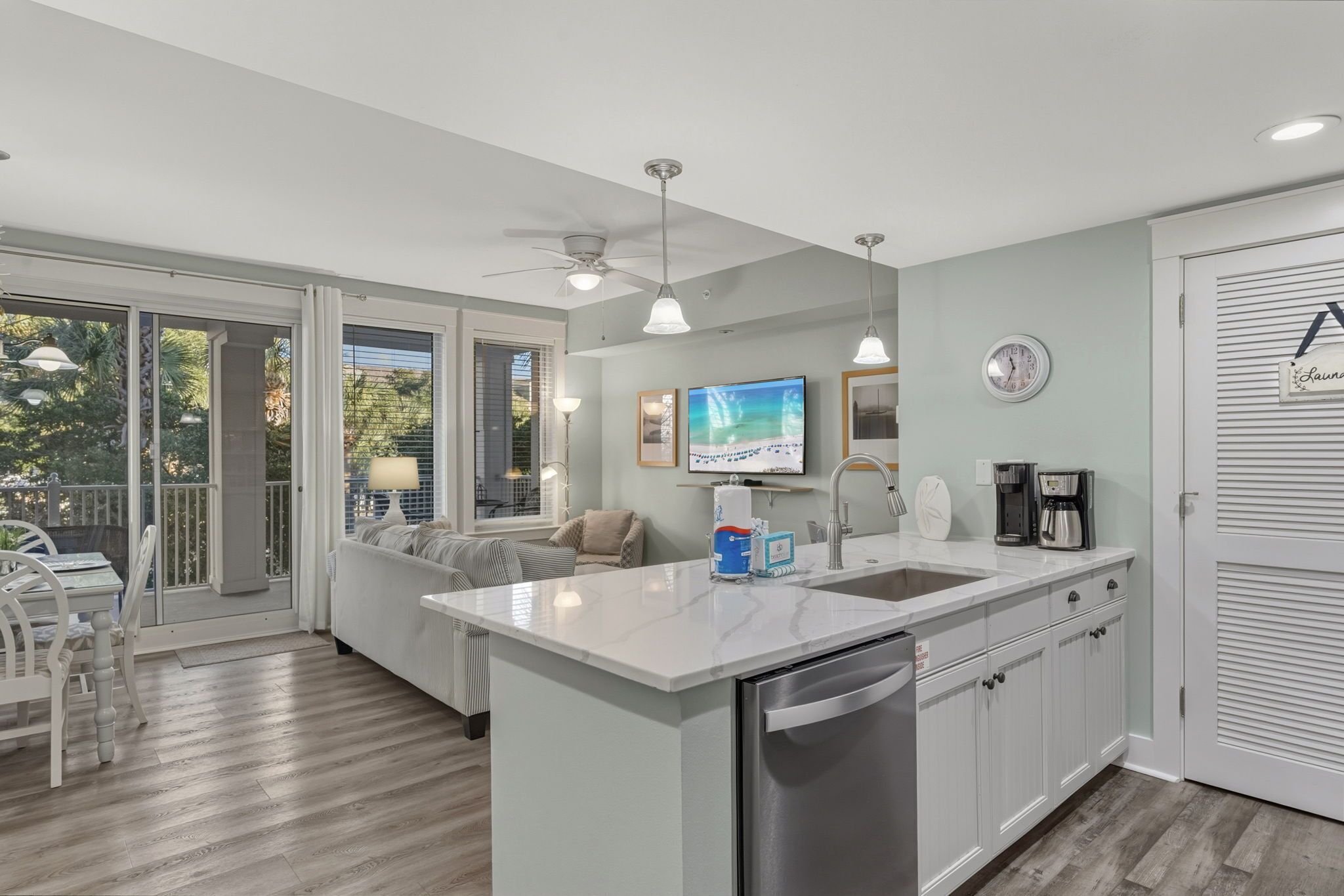 A modern kitchen with a large island, a dining area with a table and chairs, and a view through glass doors to the outside.