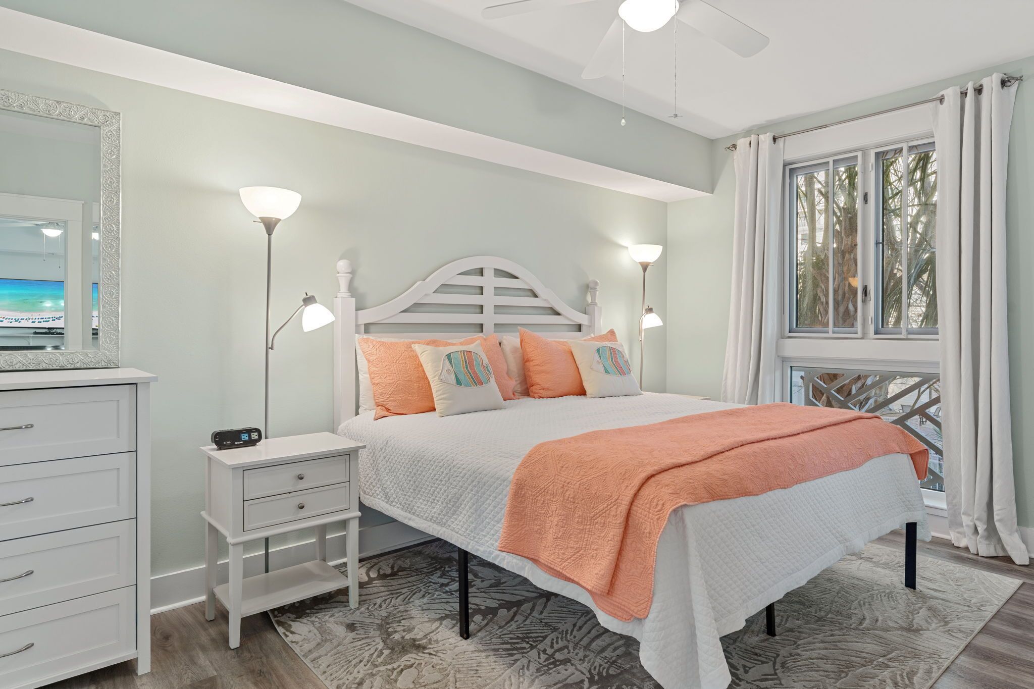 A bedroom with a bed, bedside tables, a dresser, a ceiling fan, and a window with curtains.