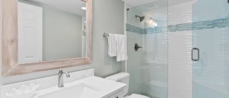 Un baño con lavamanos blanco, un espejo, inodoro y ducha con cerramiento de vidrio.