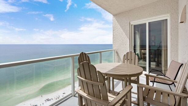 A balcony with a table and chairs, overlooking a beach and the ocean.