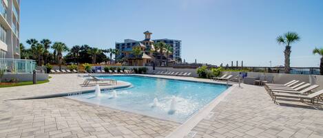 A swimming pool with a fountain, surrounded by lounge chairs and palm trees.