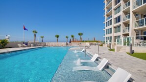 A swimming pool with lounge chairs, palm trees, and a building with balconies.