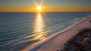 A beach with a sunset over the ocean, sandy shore, and a small structure on the right.