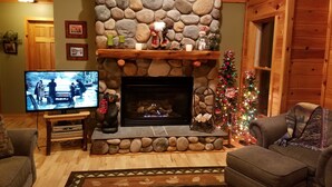 Een gezellige woonkamer met een stenen openhaard, een televisie en een kerstboom.