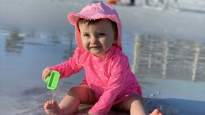 A child sitting on a beach with a clear view of the ocean and palm trees in the background. - Crystal Beach Condo Destin FL steps to private beach entrance heated pool🏝️☀️⛱️ (Destin)