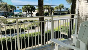 A balcony with a white railing, a white bench, and a view of the street and palm trees. - Crystal Beach Condo Destin FL steps to private beach entrance heated pool🏝️☀️⛱️ (Destin)
