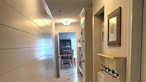 A hallway with white walls, a tiled floor, and a ceiling light fixture. - Crystal Beach Condo Destin FL steps to private beach entrance heated pool🏝️☀️⛱️ (Destin)