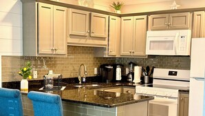 A modern kitchen with light wood cabinets, a central island with bar stools, a built-in microwave, and a double oven. - Crystal Beach Condo Destin FL steps to private beach entrance heated pool🏝️☀️⛱️ (Destin)