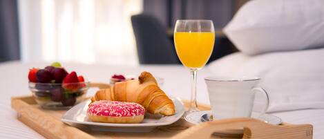 A breakfast tray with croissants, a glass of orange juice, a cup, and a bowl of fruit on a bed.