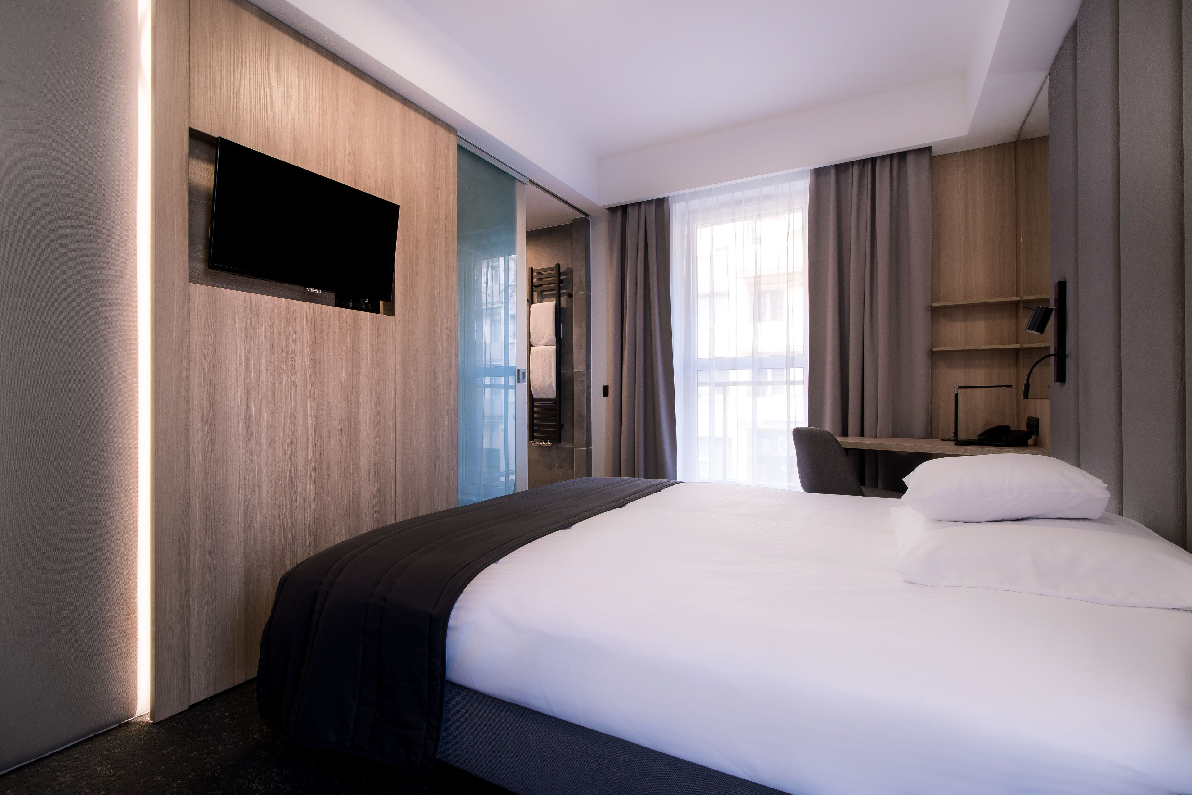 Quarto de hotel moderno com uma cama grande, televisão de tela plana na parede, escrivaninha com cadeira e janela com cortinas.