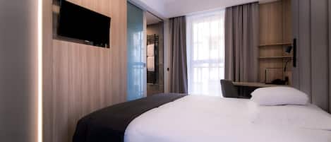 A modern hotel room with a large bed, a flat-screen TV mounted on the wall, a desk with a chair, and a window with curtains.
